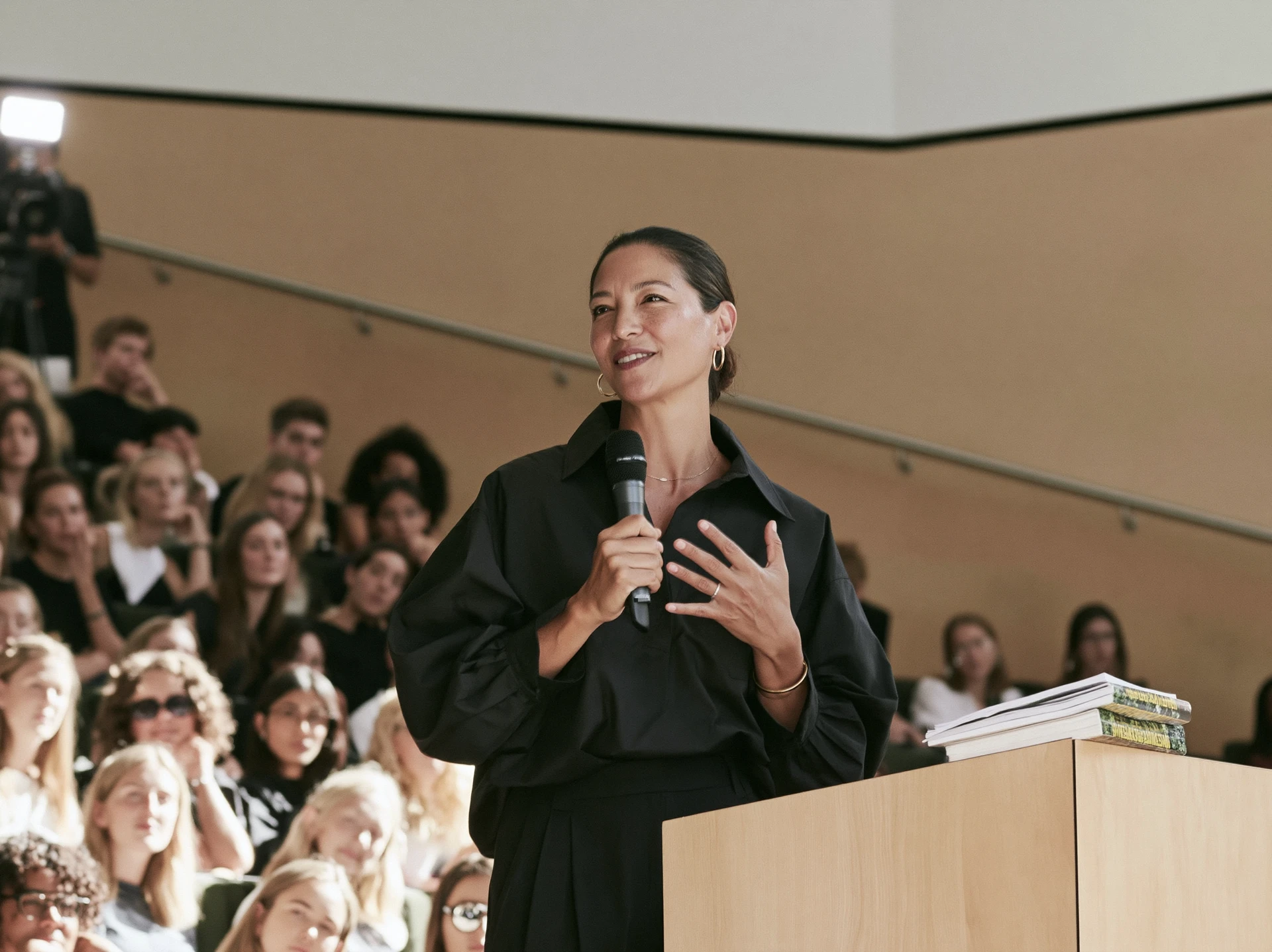 Woman speaking confidently into a microphone at a lectern before a full auditorium