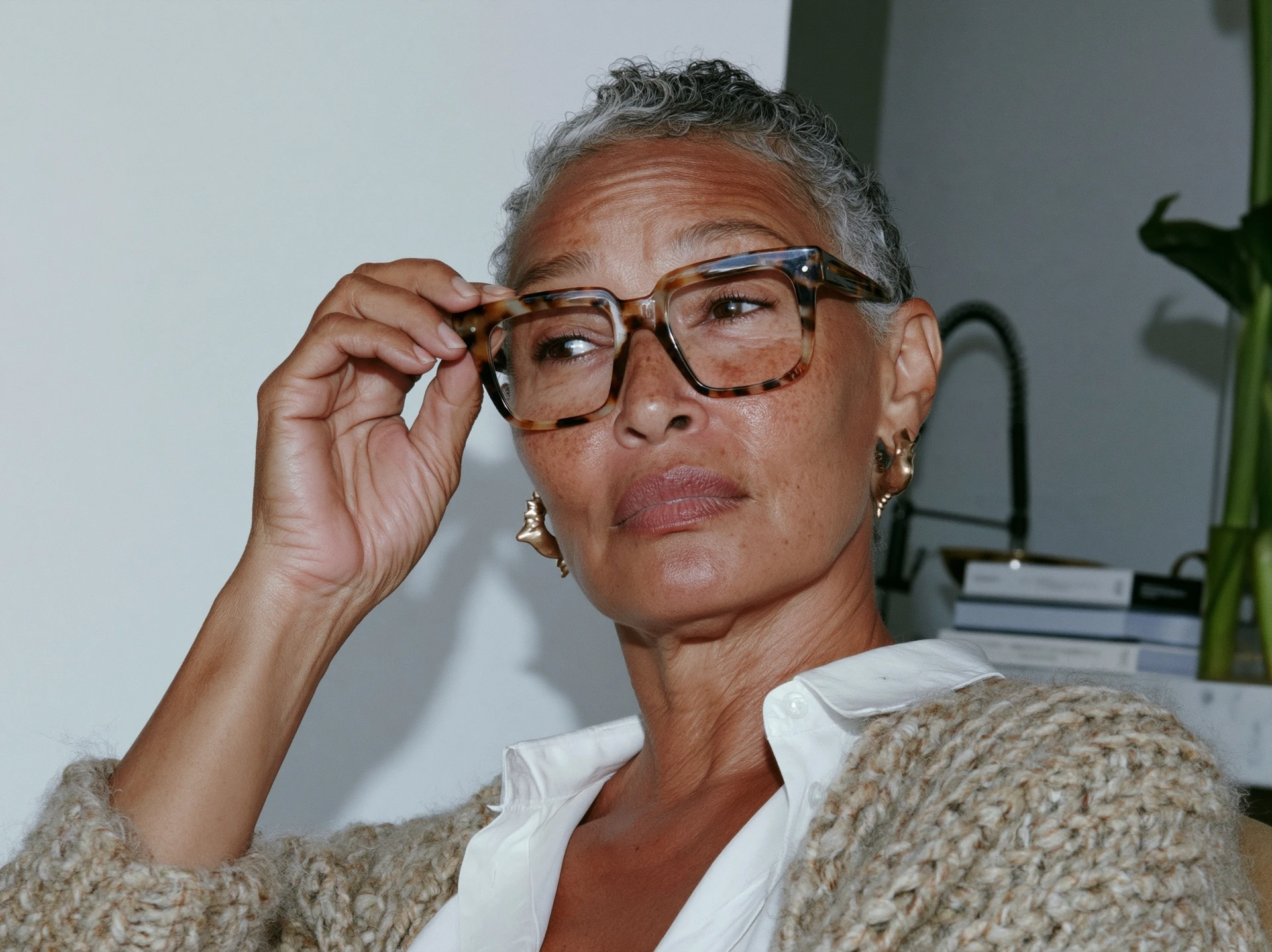 Silver-haired woman adjusting her tortoiseshell glasses, looking to the side in thought